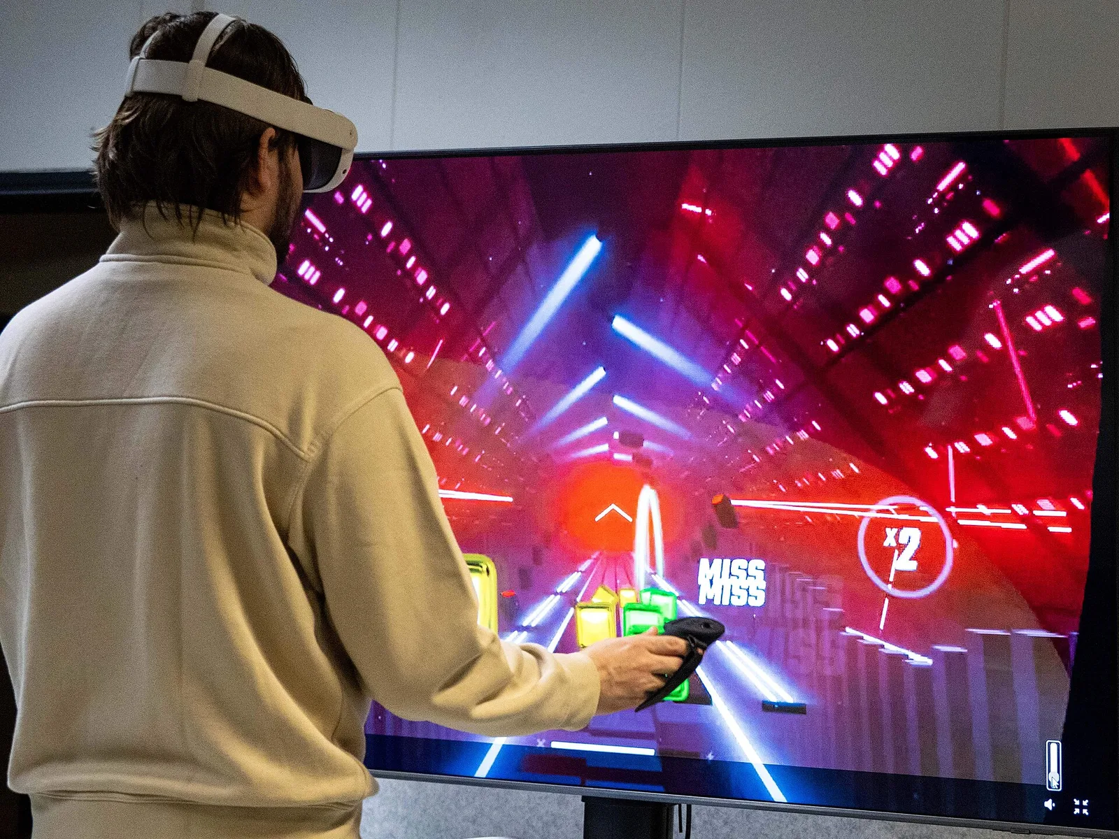 Una persona juega a Beat Saber con unas gafas de realidad virtual mientras la partida se ve en una pantalla