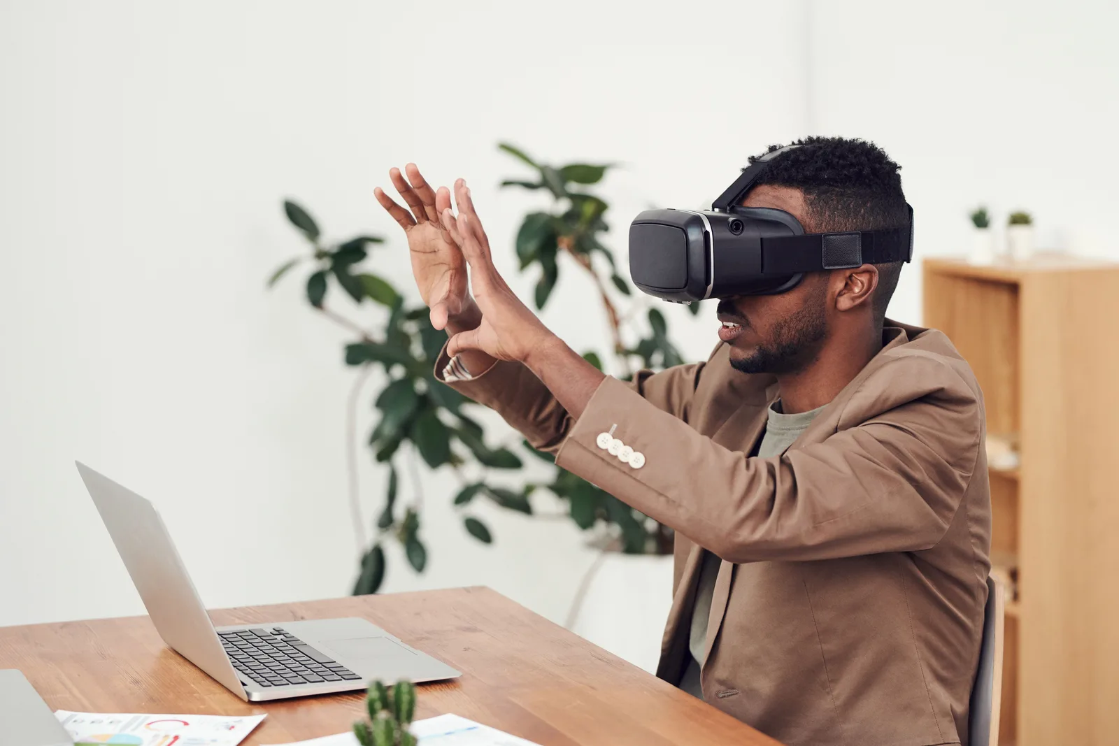 Un hombre con gafas de realidad virtual en una oficina, junto a un ordenador portátil